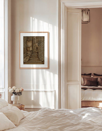 Framed print of vintage style ink drawing depicting stone buildings in Saint-Paul de Vence, France hanging in a bedroom